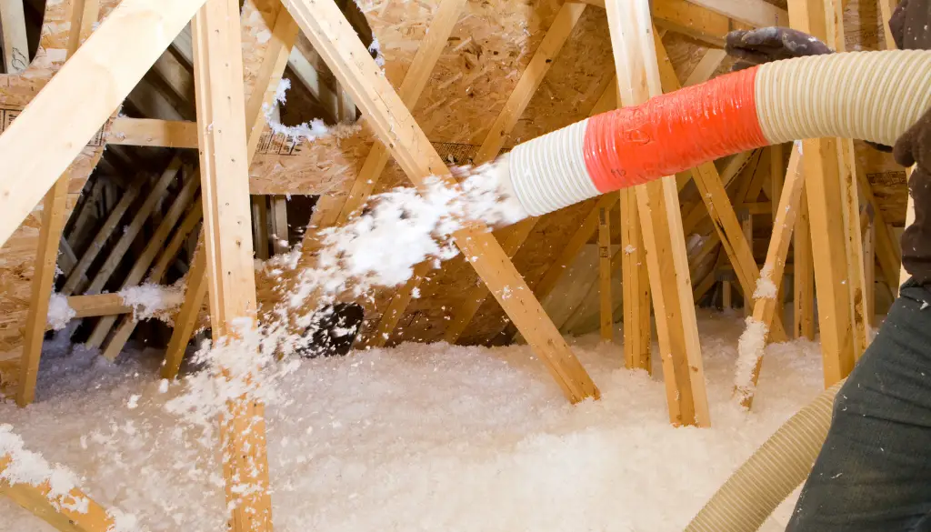Attic spray foam insulation being applied with a hose in a residential attic space.