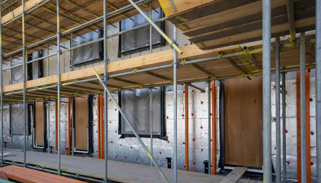 Metal building under construction with spray foam insulation applied to exterior walls, surrounded by scaffolding.