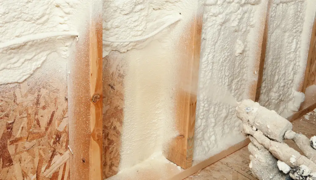 Spray foam insulation being applied to wooden wall framing in a residential construction project